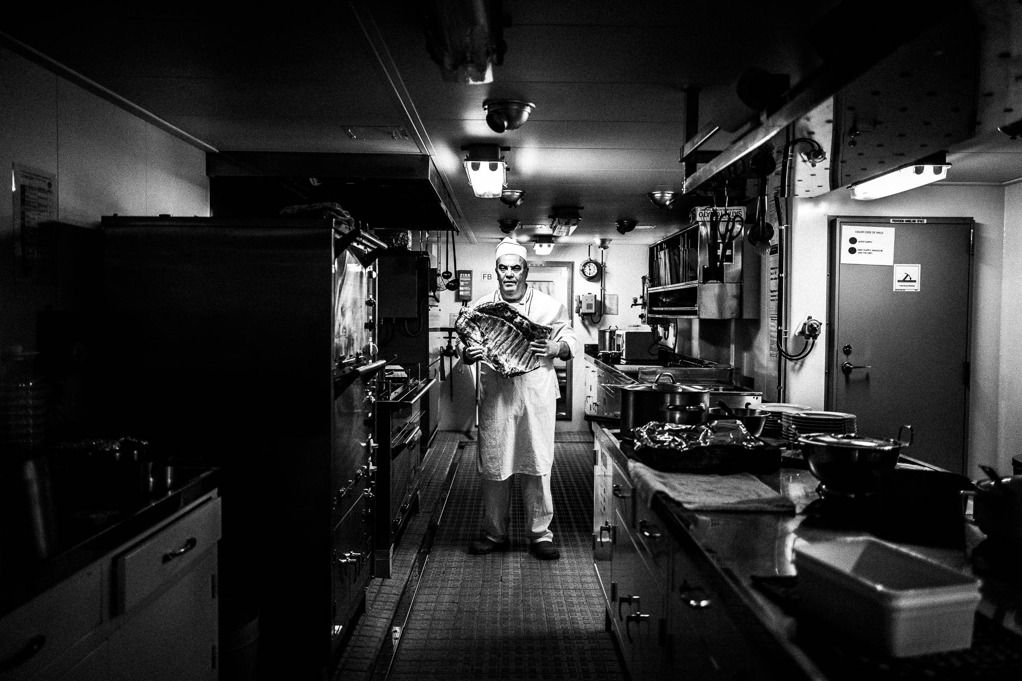The cook holding a chunk of meat in the galley by photographer George Tatakis