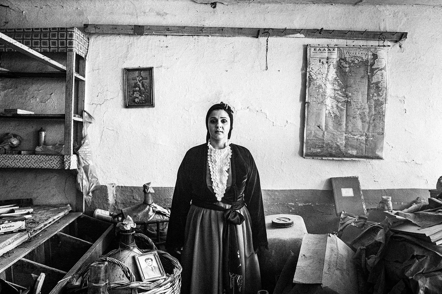 A woman inside a local abandoned shop, wearing the traditional urban dress of Pelion, Thessaly, Greece. Black and white photography by George Tatakis