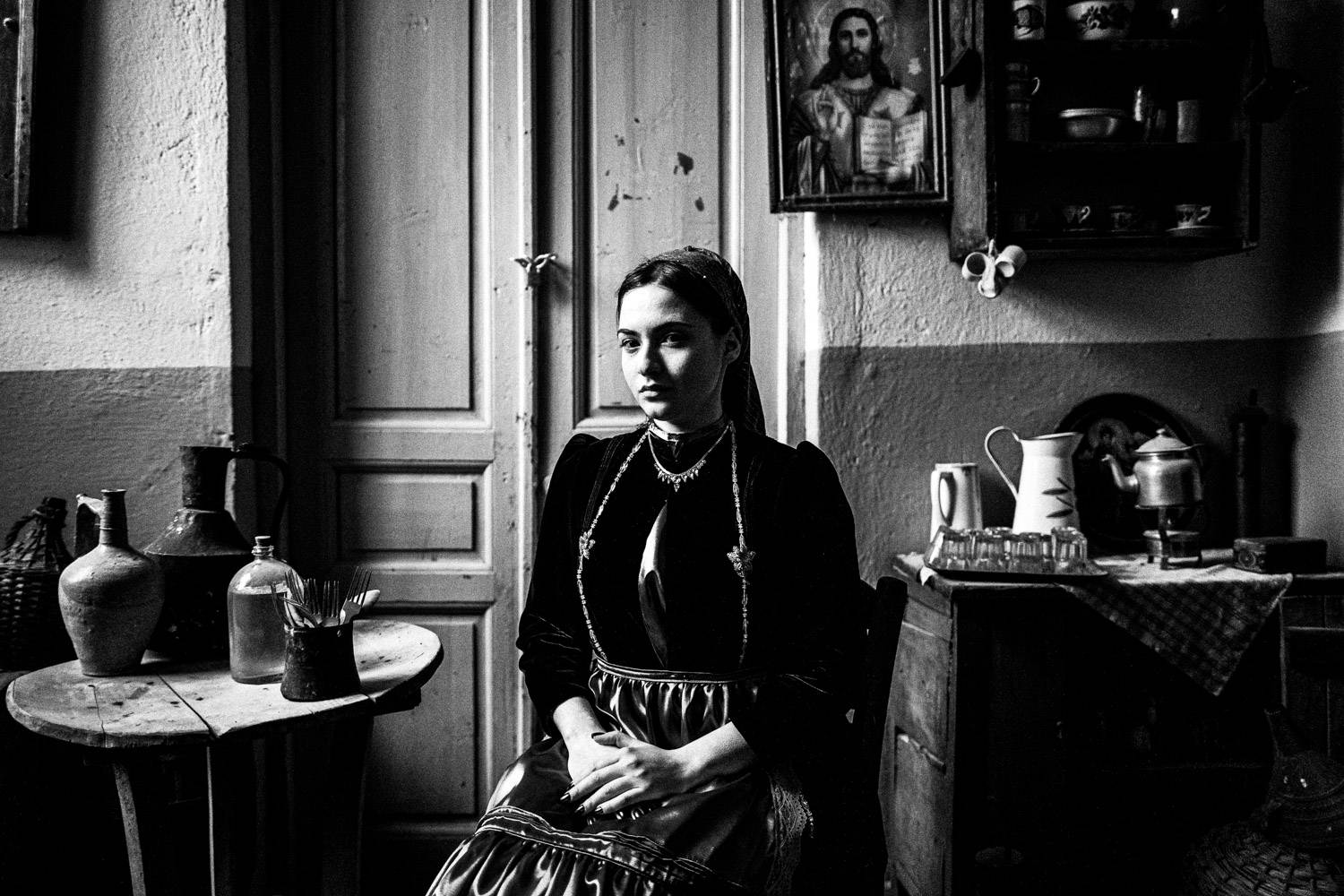 Sitting portrait of a woman wearing the traditional attire, inside the local folklore museum. Polypotamos, Florina, Macedonia, Greece. Black and white photograph by George Tatakis