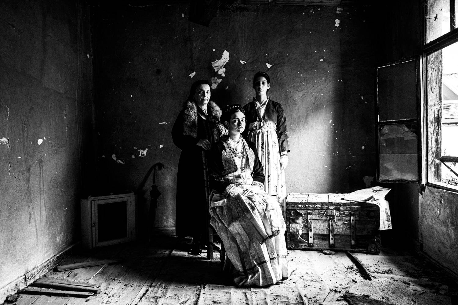 Posed portrait of three women inside a local abandoned home, wearing the traditional urban dresses of Veria, Imathia, Macedonia, Greece. Black and white photograph by George Tatakis