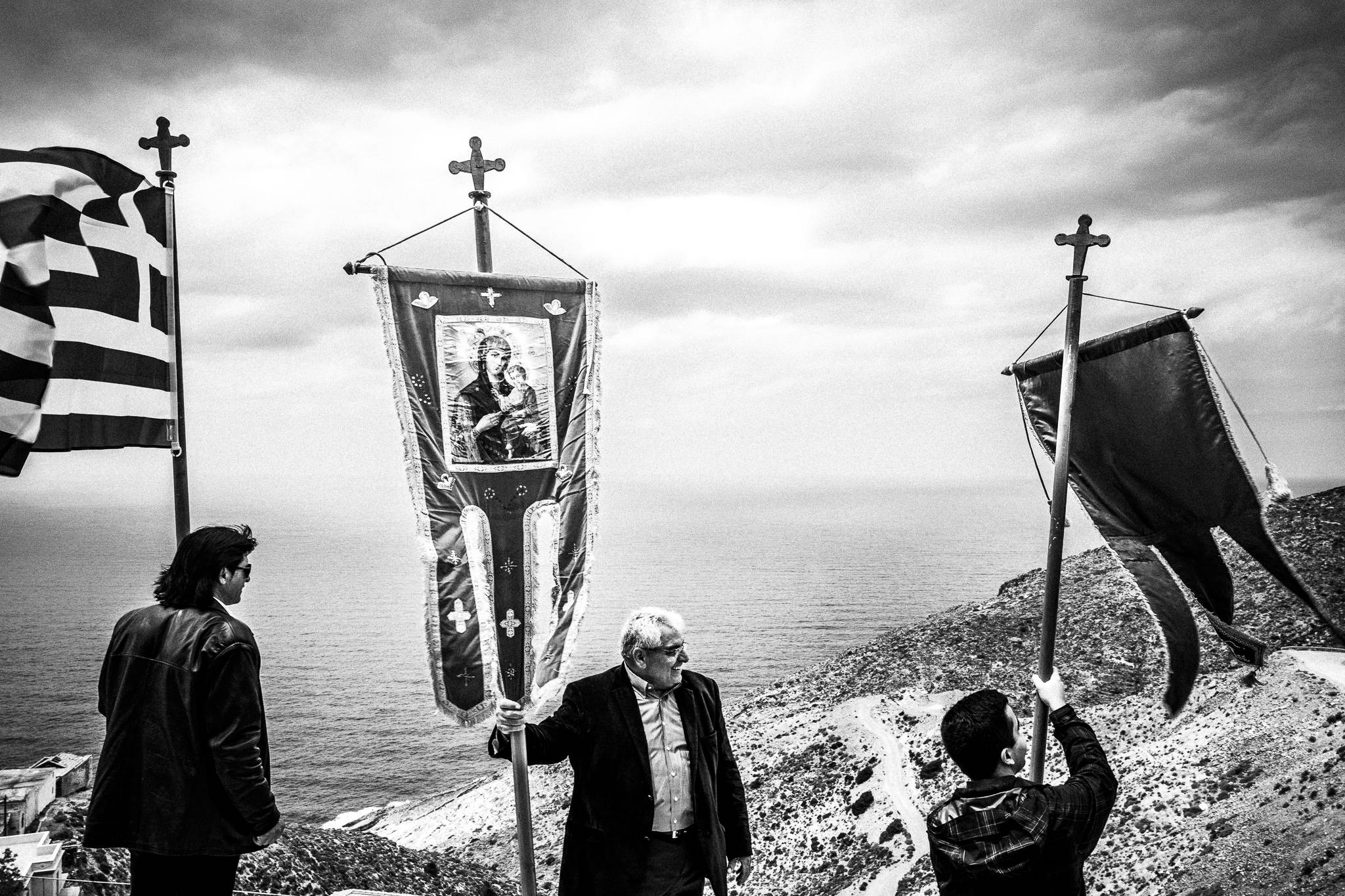 Three men holding the Greek flag and Orthodox banners, overlooking the Arhipelagos. Olympos, Karpathos, Greece. 
