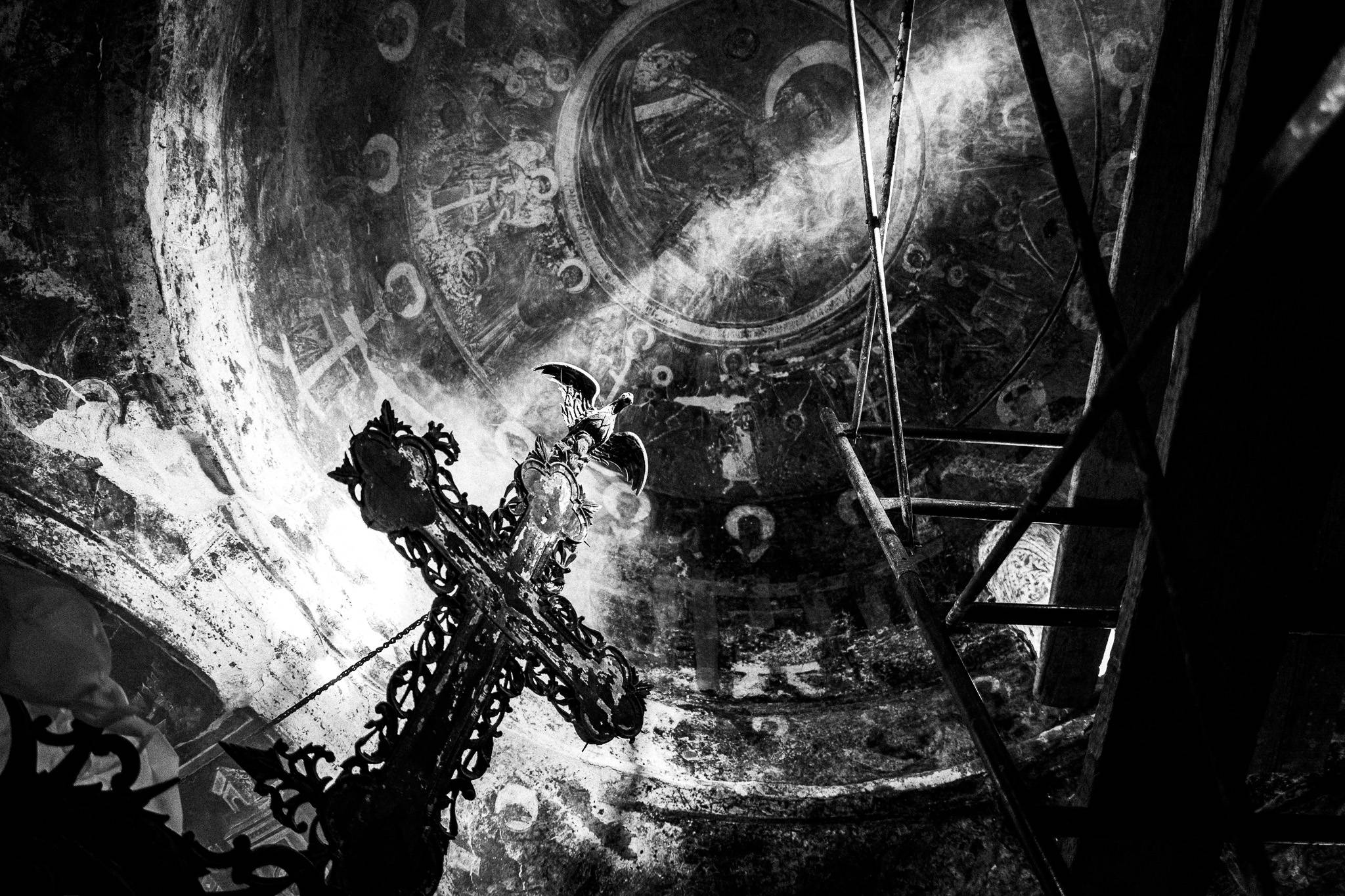 Black and white image of a decorated cross and ladder inside a mural-covered dome. Light beams enhance the intricate, historic atmosphere.