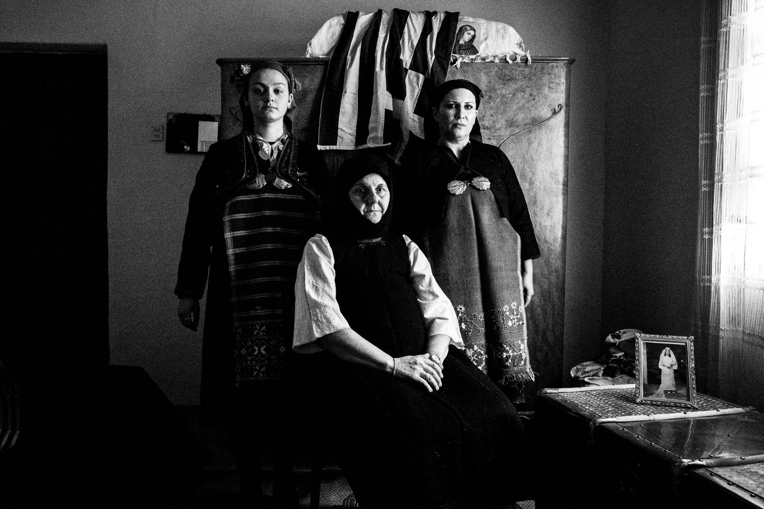 Portrait of three women wearing the Kostellides costumes, inside a local traditional home. Meliki, Imathia, Macedonia, Greece. Black and white photograph by George Tatakis