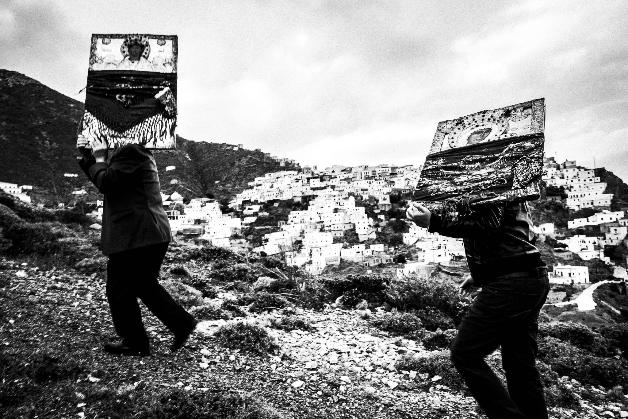 Two men, carrying heavy Orthodox Icons across the local hills overlooking the village. Easter Tuesday. Olympos, Karpathos, Greece. 