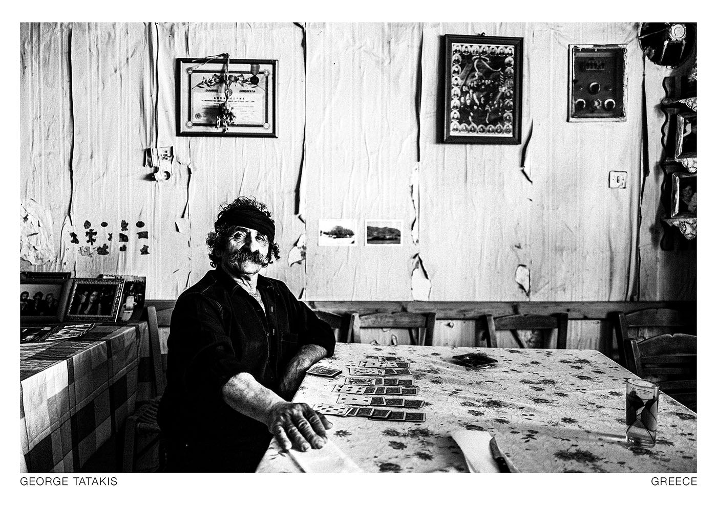 Lefteris, a local cafe owner in his shop, plays solitaire. Anogia, Rethymnon, Crete island, Greece. Black and white photography postcard by George Tatakis, project Ethos.