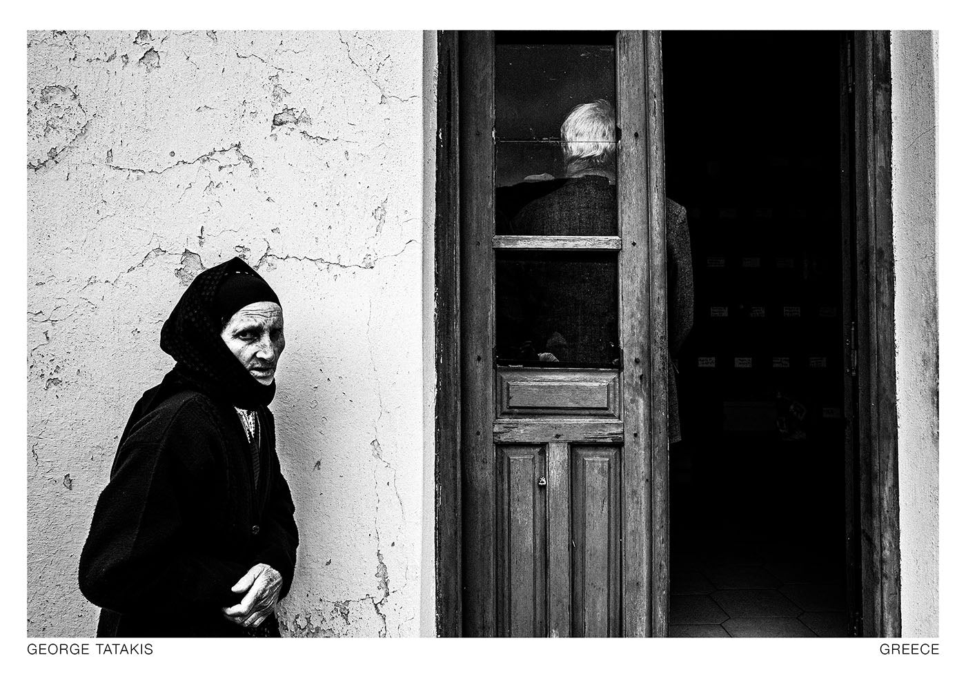 A woman standing outside the local ossuary in the village of Olympos, during Easter Tuesday. Karpathos, Greece. Black and white photography postcard by George Tatakis, project Ethos.