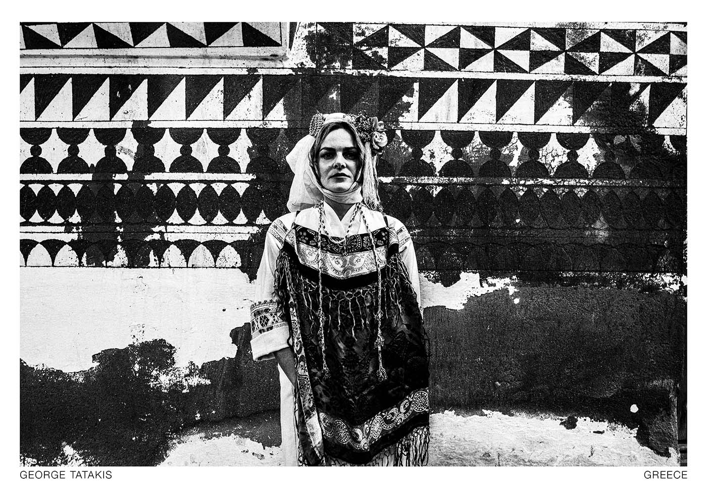 A woman standing against a plaster wall decorated with the "Xisto" technique, in the local attire of the mastic-producing village of Pyrgi, on the island of Chios, greece. Black and white photography postcard by George Tatakis, project Caryatis.