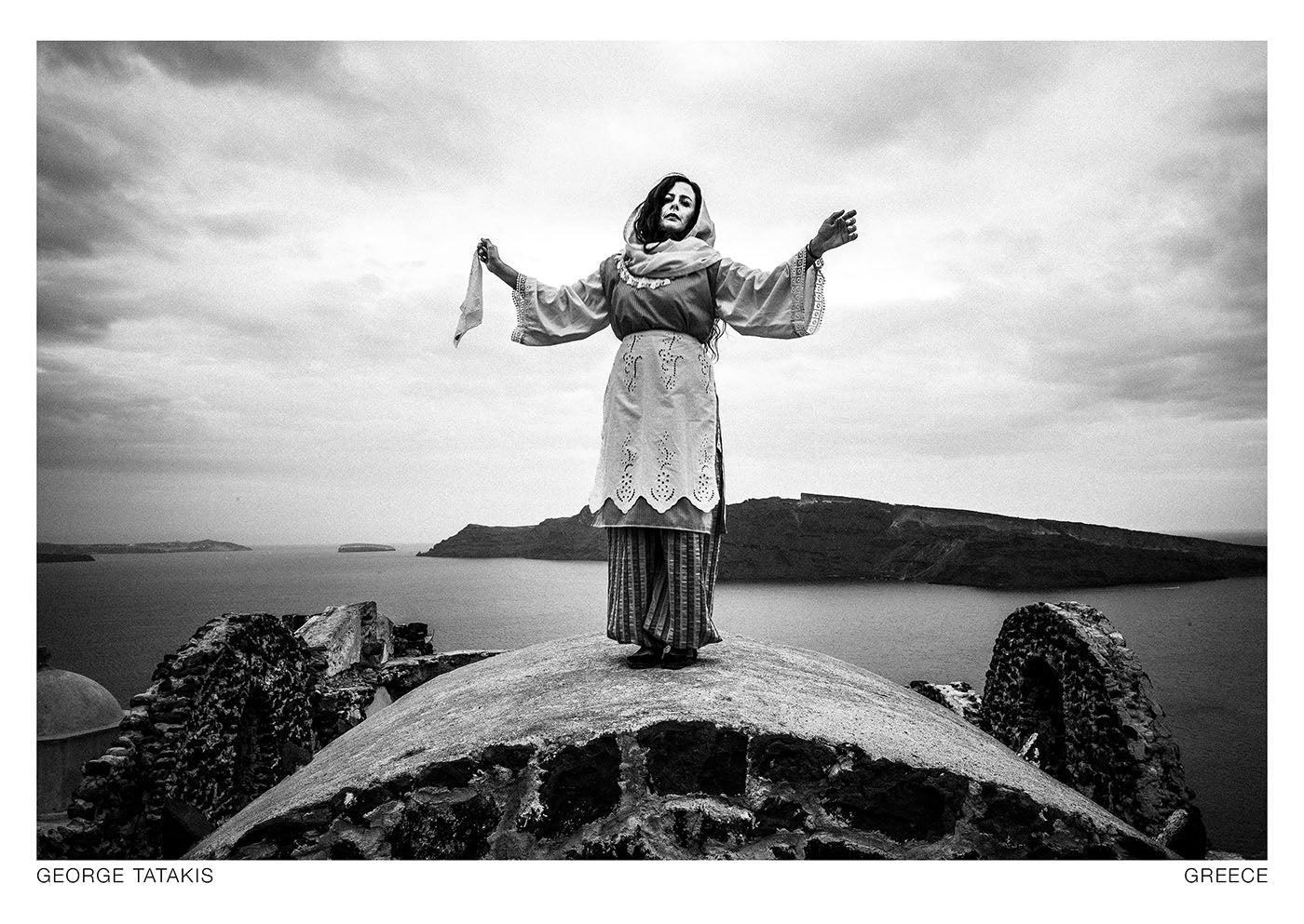 A woman standing on top of a dome, overlooking the caldera, Oia, Santorini, Cyclades. Black and white photography postcard by George Tatakis, project Caryatis.