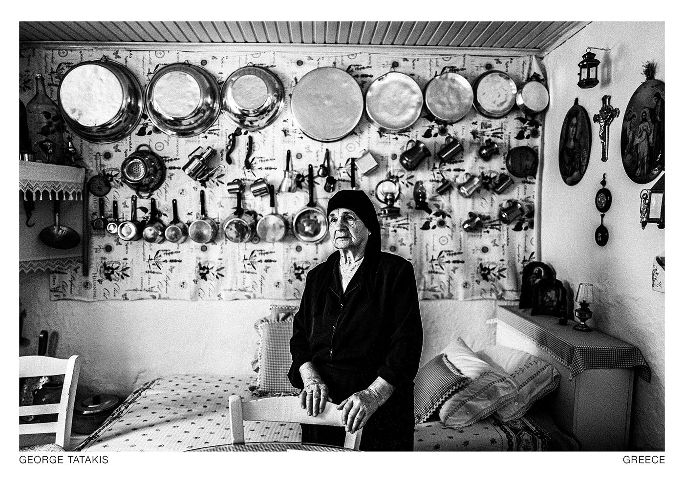 An elderly woman is posing inside her kitched, wearing traditional black Greek clothes, in Anogia, Crete, Greece. Black and white photography postcard by George Tatakis, project Ethos.