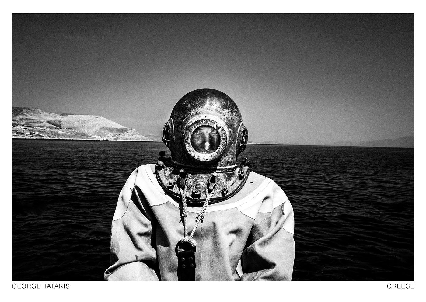 A man wearing the traditional sponge diving suit in front of the sea, Kalymnos, Dodecanese, Greece. Black and white photography postcard by George Tatakis, project Ethos.