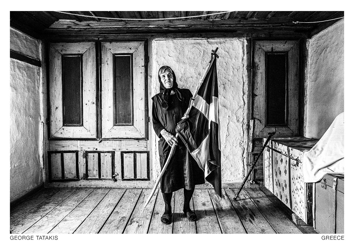 Inside her home at Metaxades, Evros, Thrace, the woman holds her Greek flag in her hands. Black and white photography postcard by George Tatakis, project Caryatis.